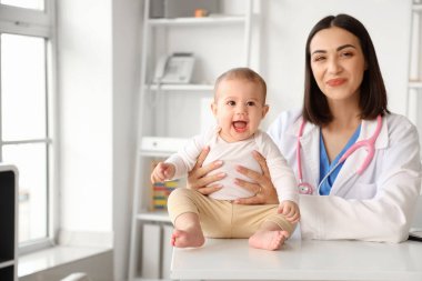 Female pediatrician with little baby at table in clinic