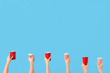 Hands holding buckets with popcorn and drinks on blue background