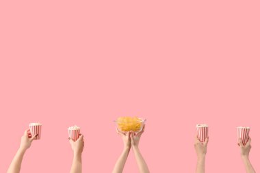 Hands holding buckets with popcorn and potato chips on pink background