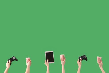 Hands holding buckets with popcorn, tablet computer and game pads on green background