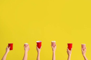 Hands holding buckets with popcorn and drinks on yellow background