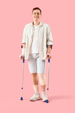 Pembe arka planda koltuk değnekleriyle kazadan sonra yaralanan genç adam.