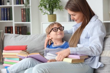 Annesi kanepede kitap okuyan sevimli küçük bir çocuk.