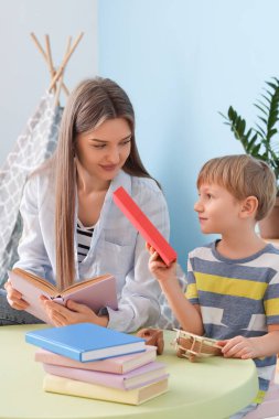 Anne ve oğlu farklı kitaplarla çocuk odasında oturuyorlar.