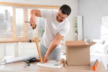 Young man with tape measure assembling table in bedroom