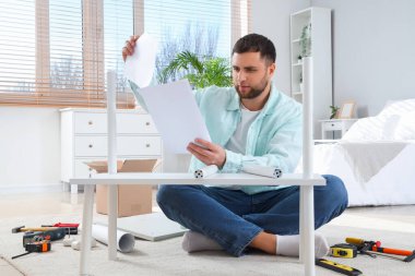 Young man with manual assembling shelf unit in bedroom