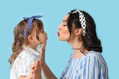 Beautiful pin-up woman kissing her daughter on blue background