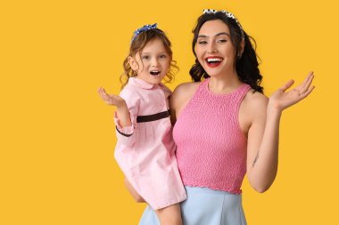 Beautiful pin-up woman and her daughter on yellow background