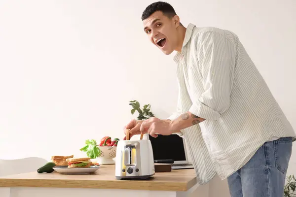 stock image Shocked young man taking burnt toasts from toaster in kitchen