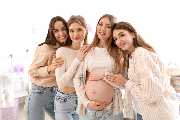 Молодая беременная женщина с друзьями, обнимающимися на вечеринке в честь рождения ребенка в спальне