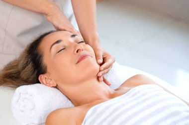 Güzel olgun bir kadın güzellik salonunda yüz masajı yaptırıyor.