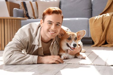 Evde yerde yatan sevimli Corgi köpeği olan kızıl saçlı mutlu genç adam.