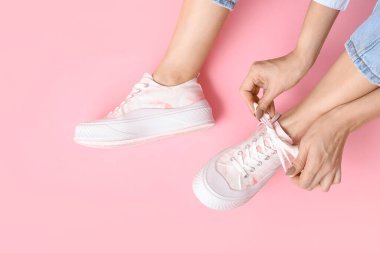 Pembe arka planda şık beyaz spor ayakkabılı genç kadın bacakları.