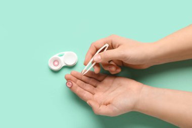 Cımbızlı kadın elleri ve turkuaz arka planda kontak lensli konteynır