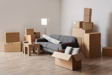 Cardboard boxes with black sofa, rolled carpet and table in living room on moving day