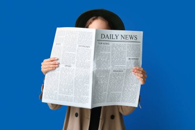 Woman in cloak and hat with newspaper on blue background