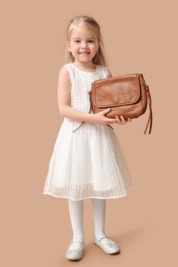 Cute little girl with stylish brown bag on color background