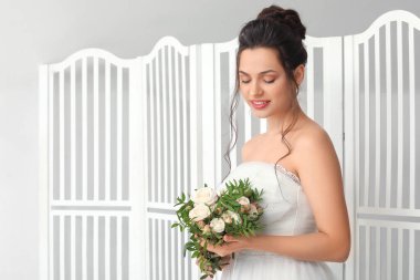 Düğün buketi olan genç gelin, arka planda katlanan perdenin yanında.