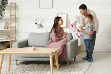 Father and son greeting his mom with Mothers Day with bouquet of flowers in living room
