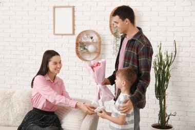 Father with son greeting his mother with Mothers Day with bouquet of tulips and gift in living room