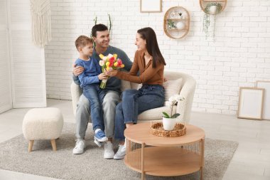 Father with son greeting his mother with Mothers Day with bouquet of tulips in living room