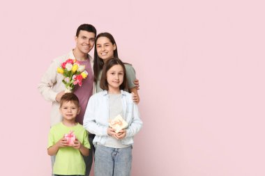 Family with bouquet of flowers and gifts near pink wall