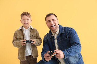 Mutlu baba ve küçük oğlu sarı arka planda video oyunu oynuyorlar.