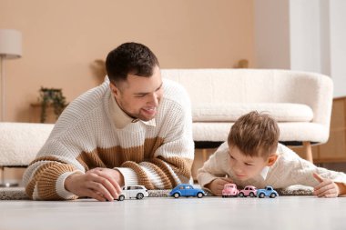 Mutlu baba ve küçük oğlu evde yerde yatıp oyuncak arabalarla oynuyorlar.