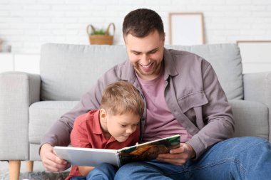 Happy father and his little son reading book together at home