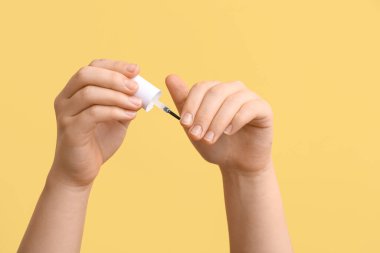Female hands holding brush with cuticle oil on yellow background, closeup