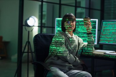 Female programmer with coffee cup and projection of programming code in office at night
