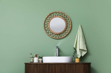 Tezgahta banyo malzemeleri ve banyoda yeşil duvarın yanında şık bir ayna olan modern lavabo.