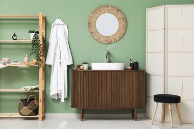 Tezgahta banyo malzemeleri ve banyoda yeşil duvarın yanında şık bir ayna olan modern lavabo.