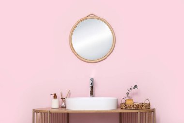 Banyodaki pembe duvarın yanındaki raflarda banyo malzemeleri olan modern lavabo.