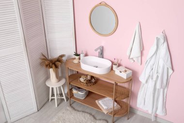 Banyodaki pembe duvarın yanındaki raflarda banyo malzemeleri olan modern lavabo.