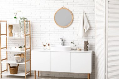 Banyodaki beyaz tuğla duvarın yanında banyo malzemeleri olan modern lavabo.