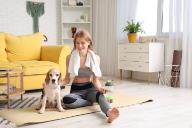 Evde yoga yaptıktan sonra sevimli Beagle köpeği ve cep telefonu olan genç bir kadın.
