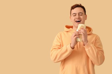 Young man eating doner kebab on beige background
