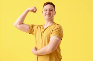 Young man with applied medical patch showing strength symbol on yellow background. Vaccination concept