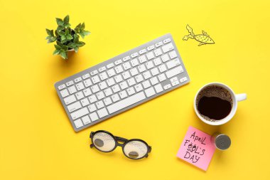 Bilgisayar klavyesi, yapışkan not, sarı arka planda tuz ve fincan kahve. 1 Nisan şakası.