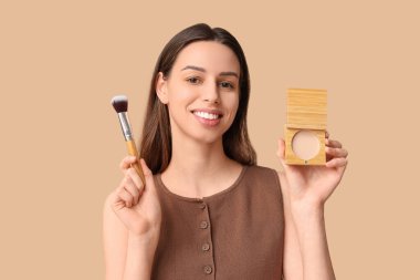 Beautiful young woman with face powder and brush on brown background