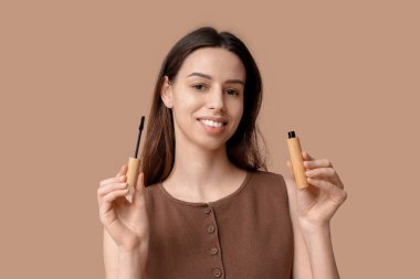 Beautiful young woman with mascara on brown background