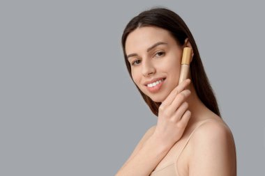 Portrait of beautiful young woman with concealer on grey background