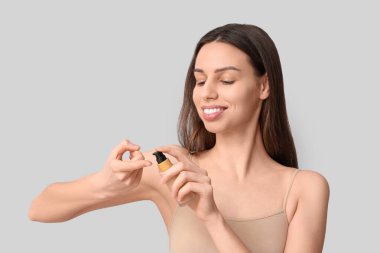 Beautiful young woman applying foundation on grey background