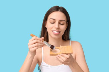 Beautiful young woman with face powder and brush on blue background