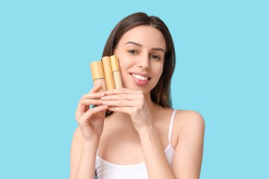Beautiful young woman holding set of decorative cosmetics on blue background