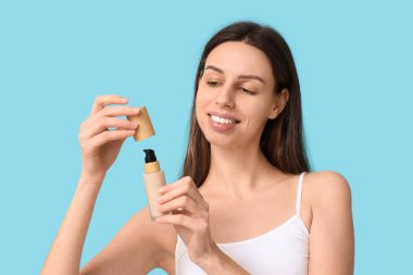 Beautiful young woman opening foundation on blue background