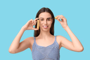 Beautiful young woman with mascara on blue background