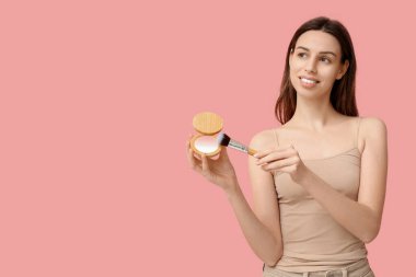 Thoughtful young woman with brush and highlighter on pink background