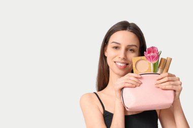 Beautiful young woman holding cosmetic bag with tulip and decorative cosmetics on white background